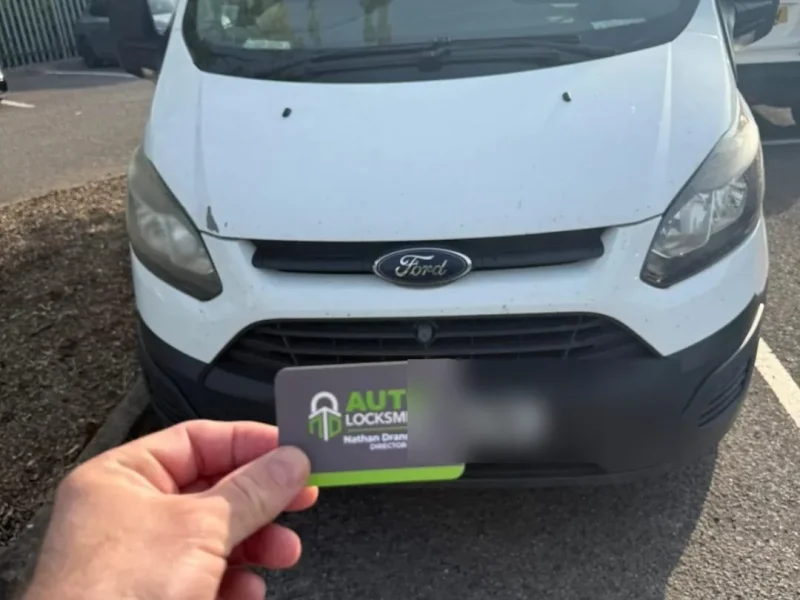 ND Auto Locksmiths business card held up in front of a white Ford Transit Custom van, number plate blurred